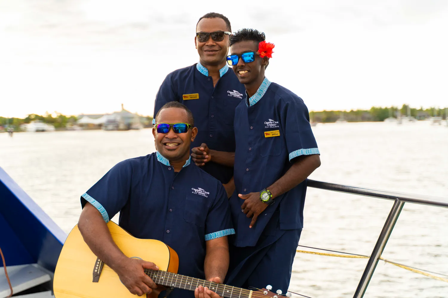 Captain Cook Fiji Entertainment Staff on Deck Three uniformed staff members from Captain Cook Cruises Fiji pose together on the deck of a vessel