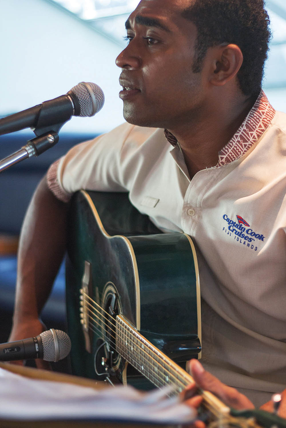 Captain Cook Islands Performance with Acoustic Guitar A musician performs with an acoustic guitar and microphone, wearing a Captain Cook Cruises Fiji
