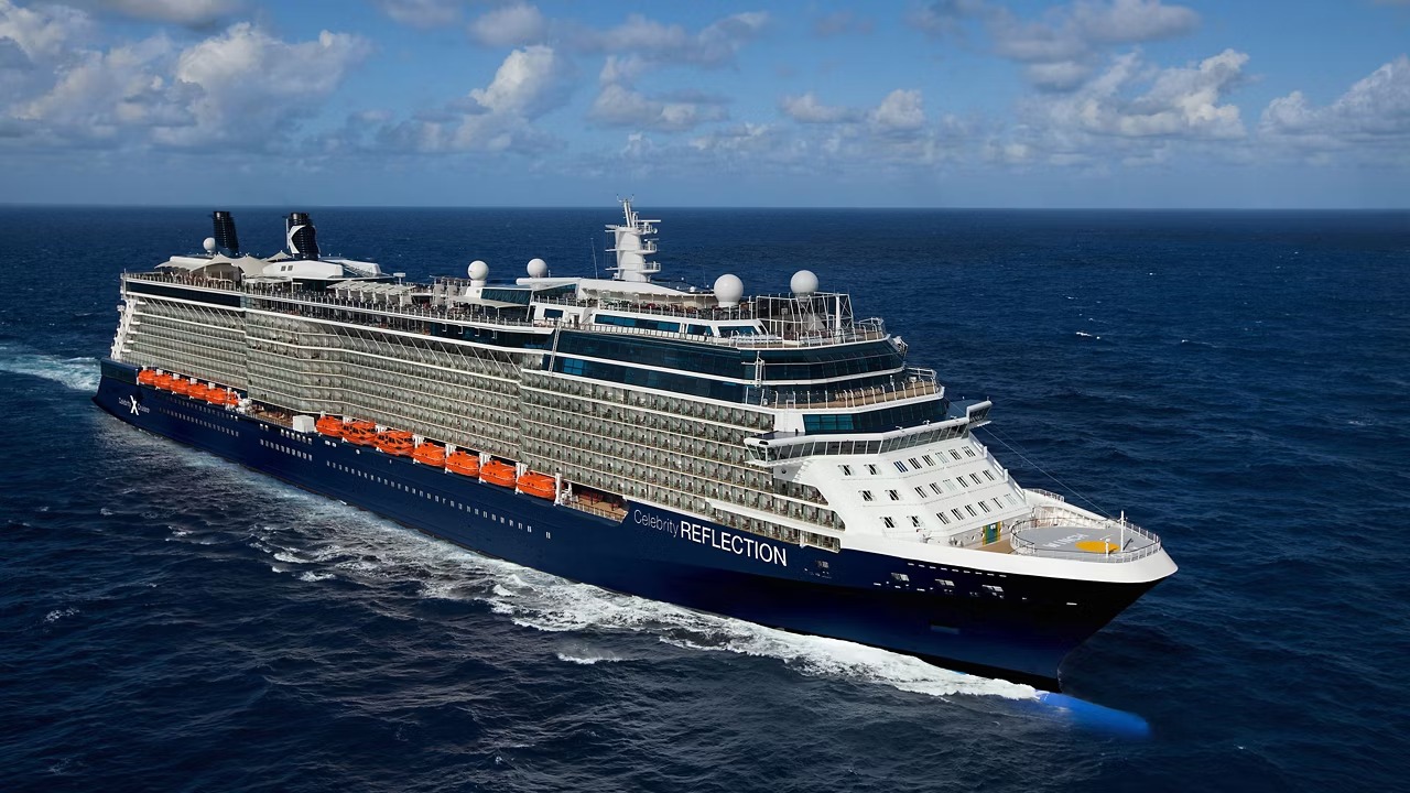 An aerial view of the Celebrity Reflection, a large modern cruise ship, sailing through open ocean