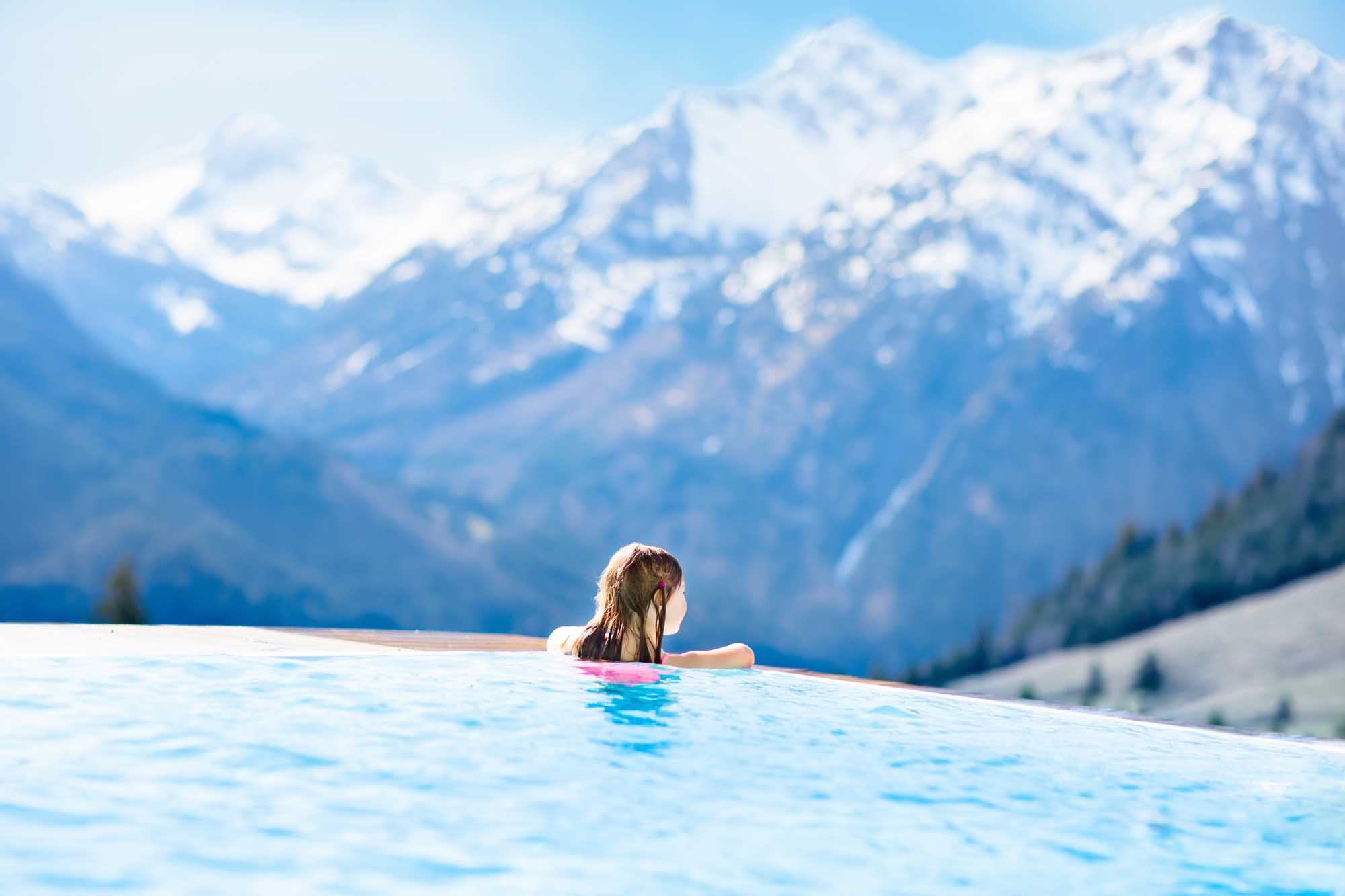 Child in Infinity Pool with Alpine Mountain Views A young child enjoys an outdoor infinity pool at a luxury Alpine resort, with snow-capped mountains