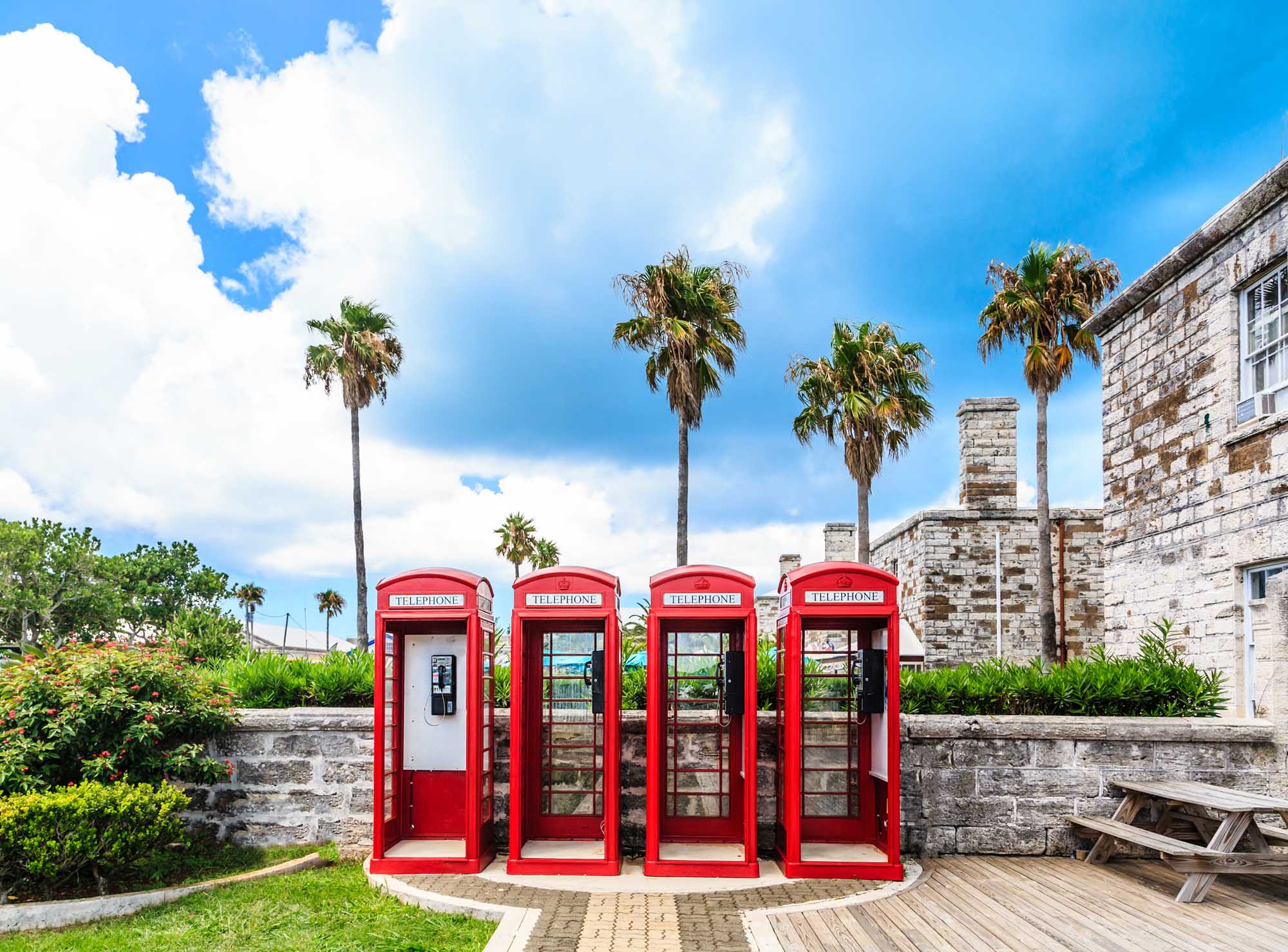 Classic British Red Phone Booths in Bermuda Four iconic red British telephone booths stand in a row against a backdrop of colonial stone