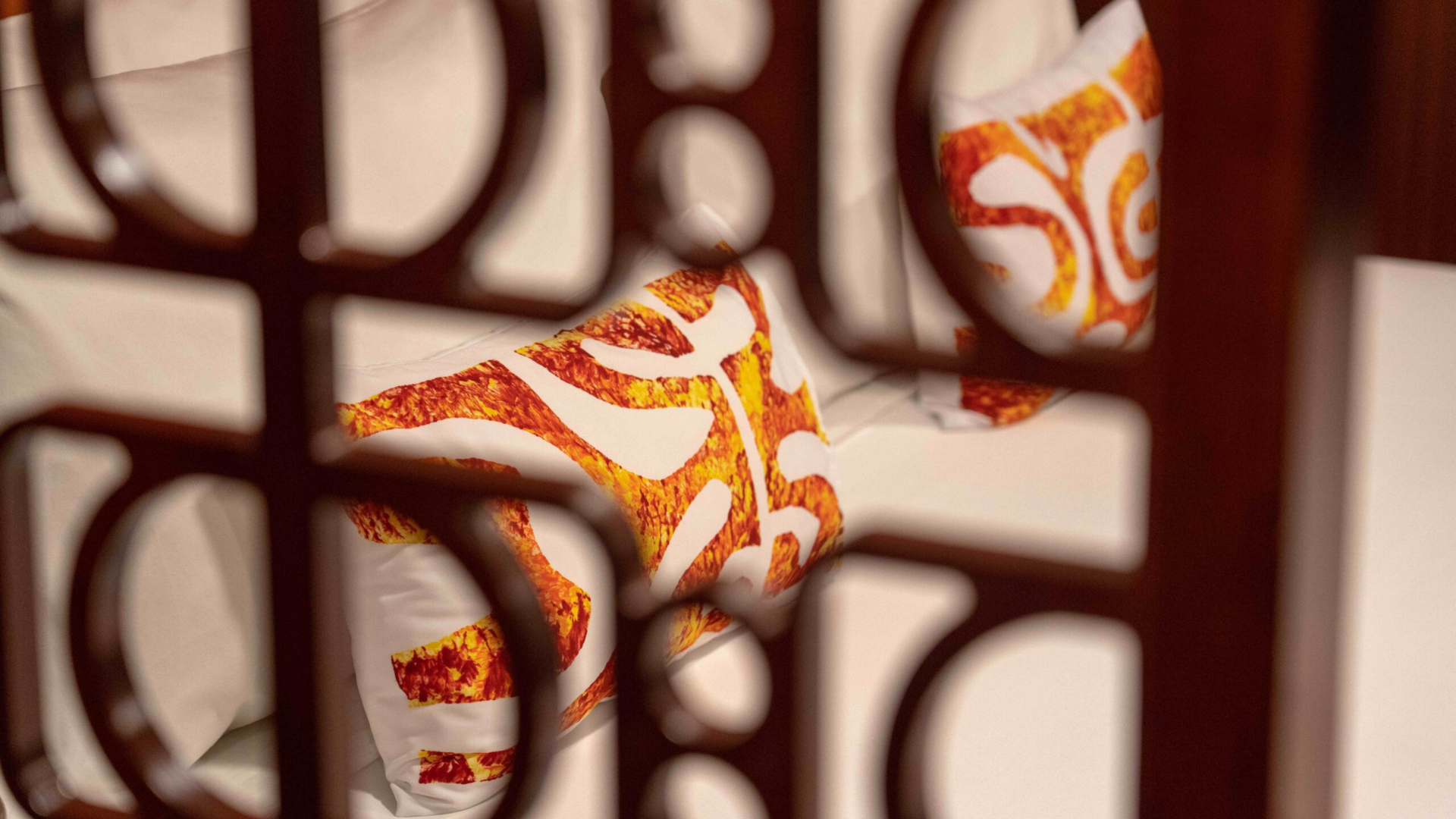 Colorful Patterned Fabric Through Ornate Railing A close-up view of vibrant red, orange, and yellow patterned fabric draped over or held against