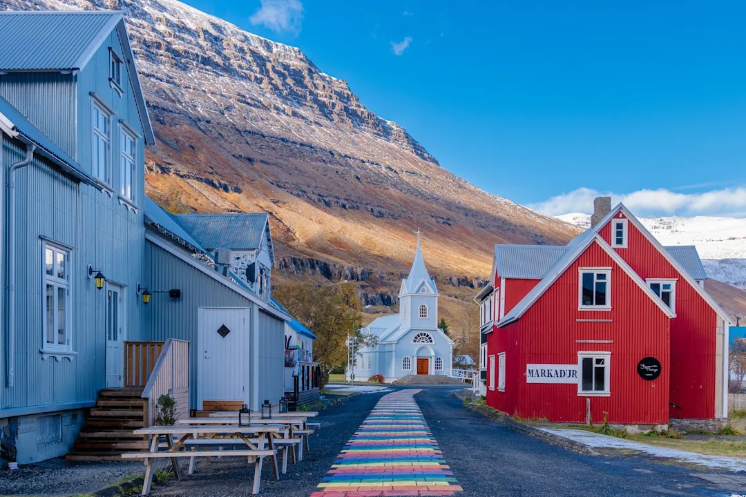 Colorful Village Church in Icelandic Fjord Valley A picturesque Icelandic village nestled beneath dramatic mountains, featuring traditional
