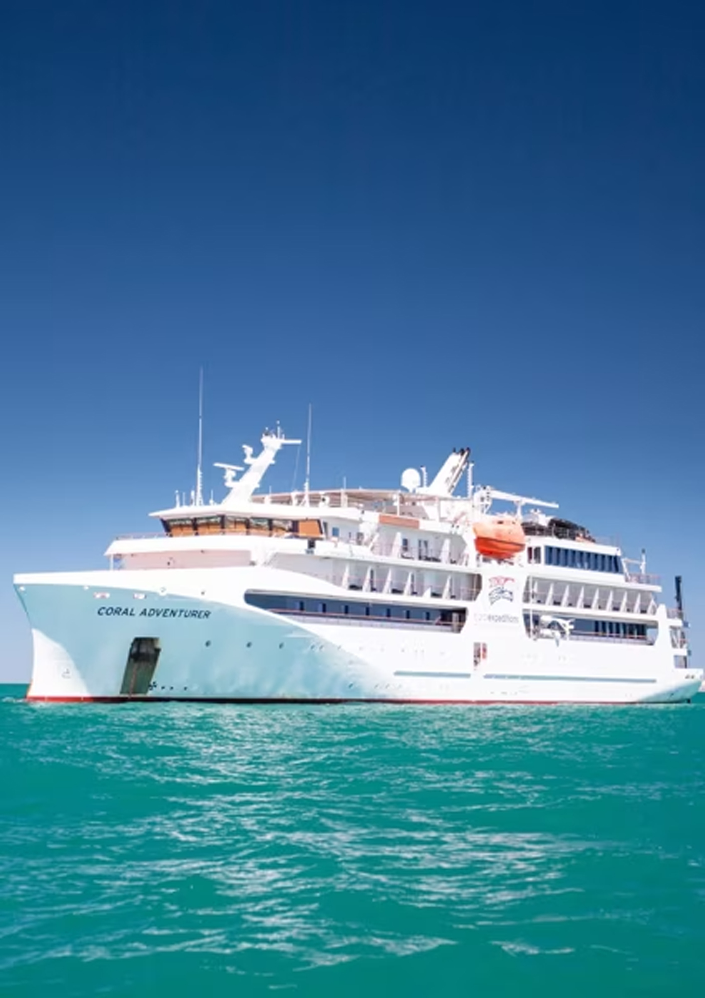 The Coral Adventurer, a modern expedition cruise ship, is pictured anchored in turquoise tropical