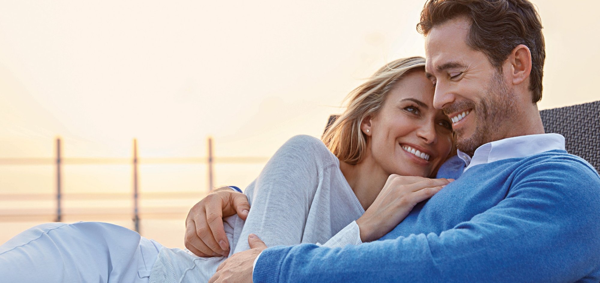 Couple Enjoying Sunset Aboard Hapag-Lloyd Cruises A romantic scene of a couple relaxing together on the deck of a cruise ship at sunset, with calm