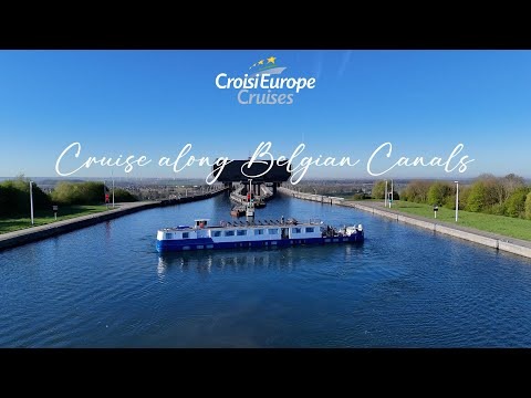 A CroisiEurope river cruise ship navigates through a scenic Belgian canal with expansive green