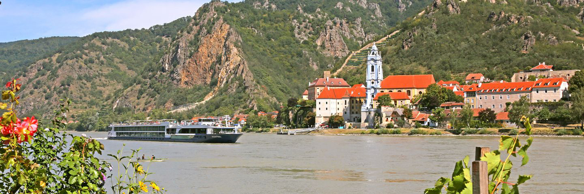 Danube River Cruise Ship at Charming Riverside Town A river cruise ship navigates the Danube River past a picturesque riverside village nestled beneath