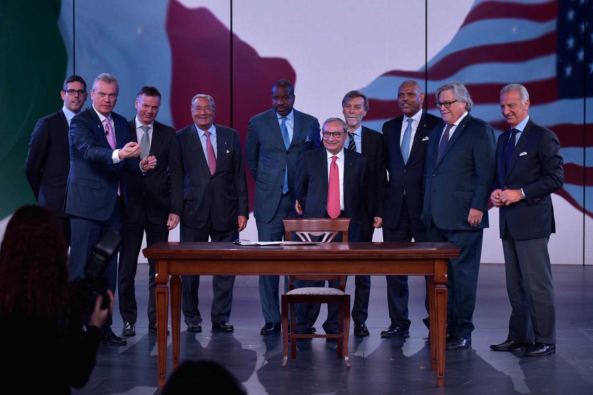 Distinguished Gentlemen at Formal Desk Ceremony A formal gathering of nine well-dressed men in business suits positioned around a wooden desk on