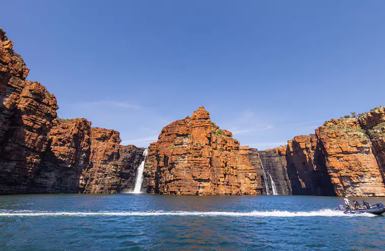 Dramatic Red Rock Cliffs and Waterfalls in Kimberley A stunning coastal landscape featuring towering red sandstone cliffs with cascading waterfalls