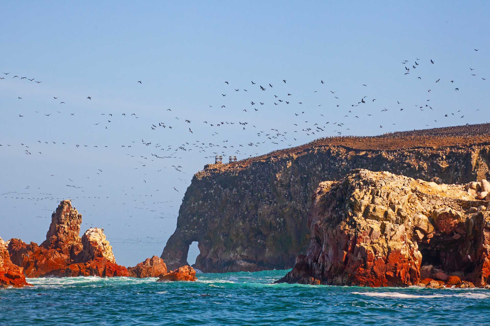 Dramatic Rock Formations at Ballestas Islands with Seabirds A stunning coastal seascape featuring towering red and golden rock formations with a distinctive