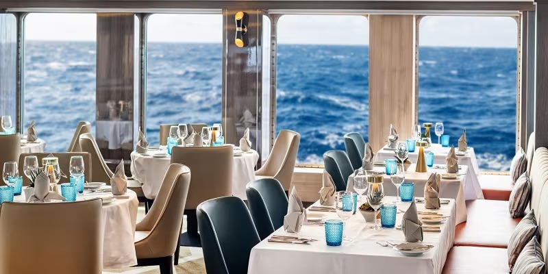 Elegant Dining with Ocean Views aboard Expedition Vessel A sophisticated restaurant dining room aboard an expedition cruise ship, featuring large