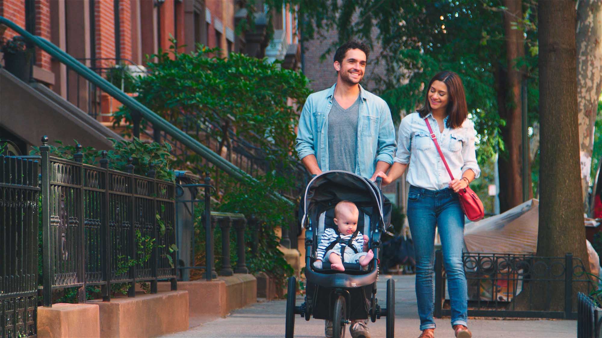 Family Stroll Through Urban Street With Baby Stroller A young family enjoys a leisurely walk through a tree-lined urban street, with the father pushing