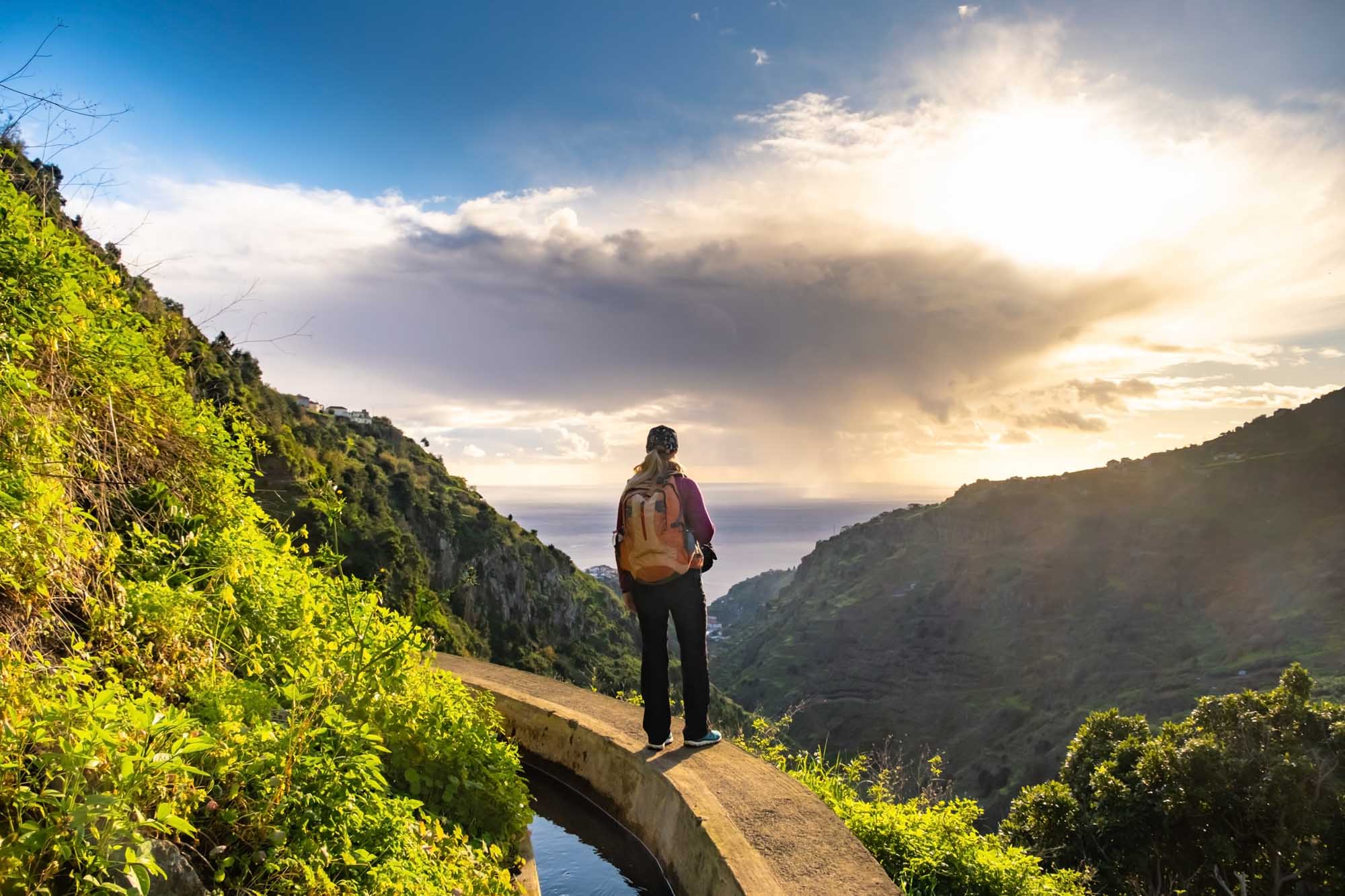Hiker on Levada do Norte Trail, Madeira A solo hiker with an orange backpack stands on a narrow concrete path alongside the Levada do Norte