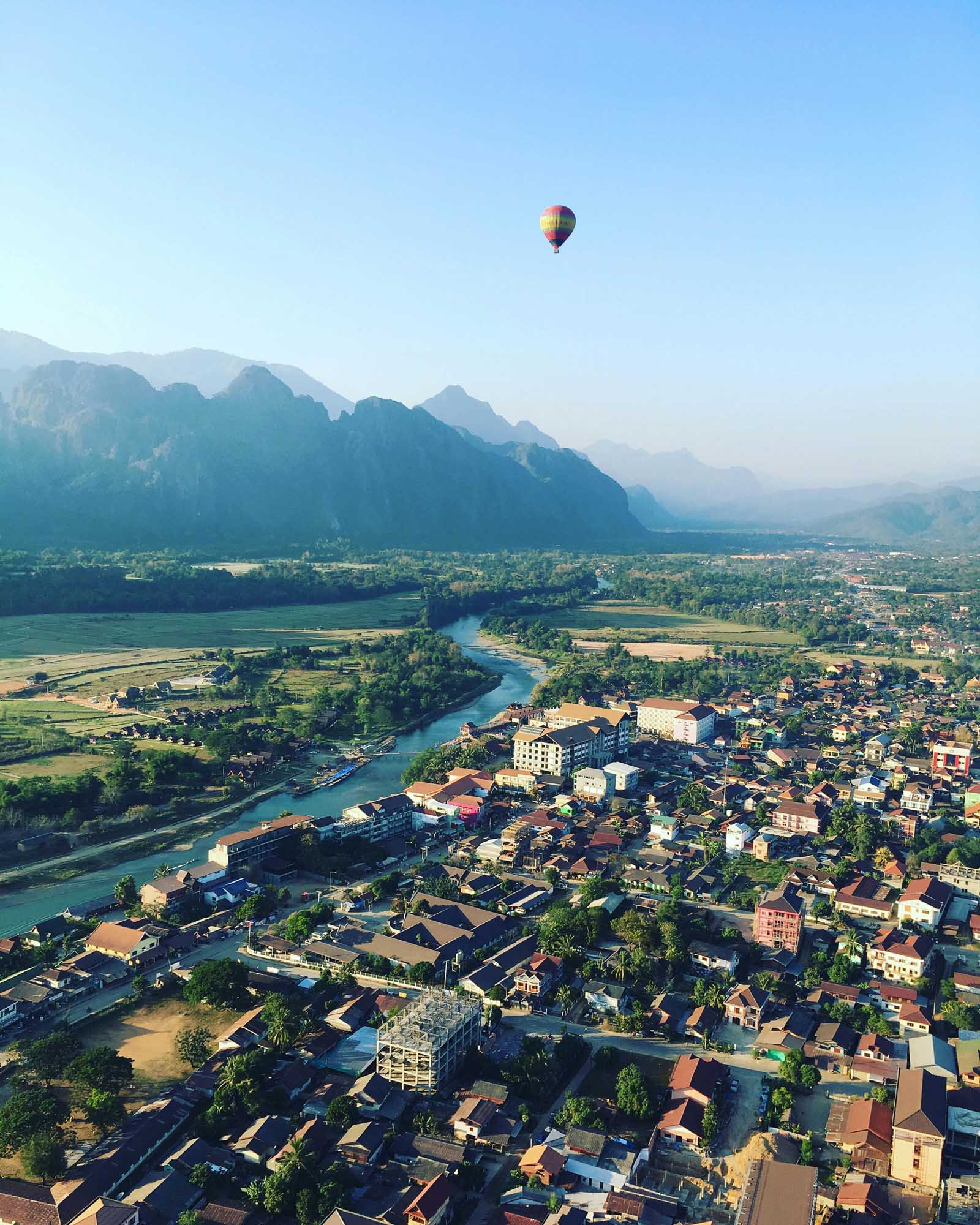 A colorful hot air balloon floats above the stunning karst landscape of Vang Vieng, Laos