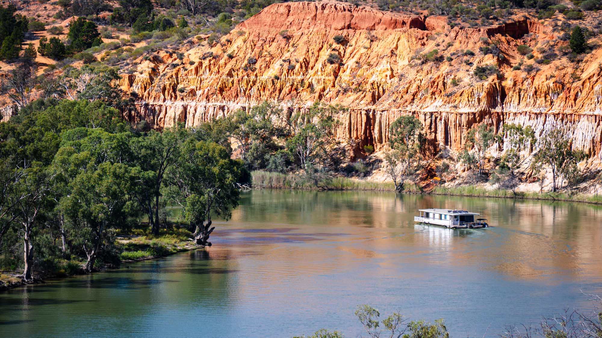 Houseboat on Murray River at Headings Cliff A serene scene on the Murray River featuring a houseboat cruising past the dramatic ochre and white