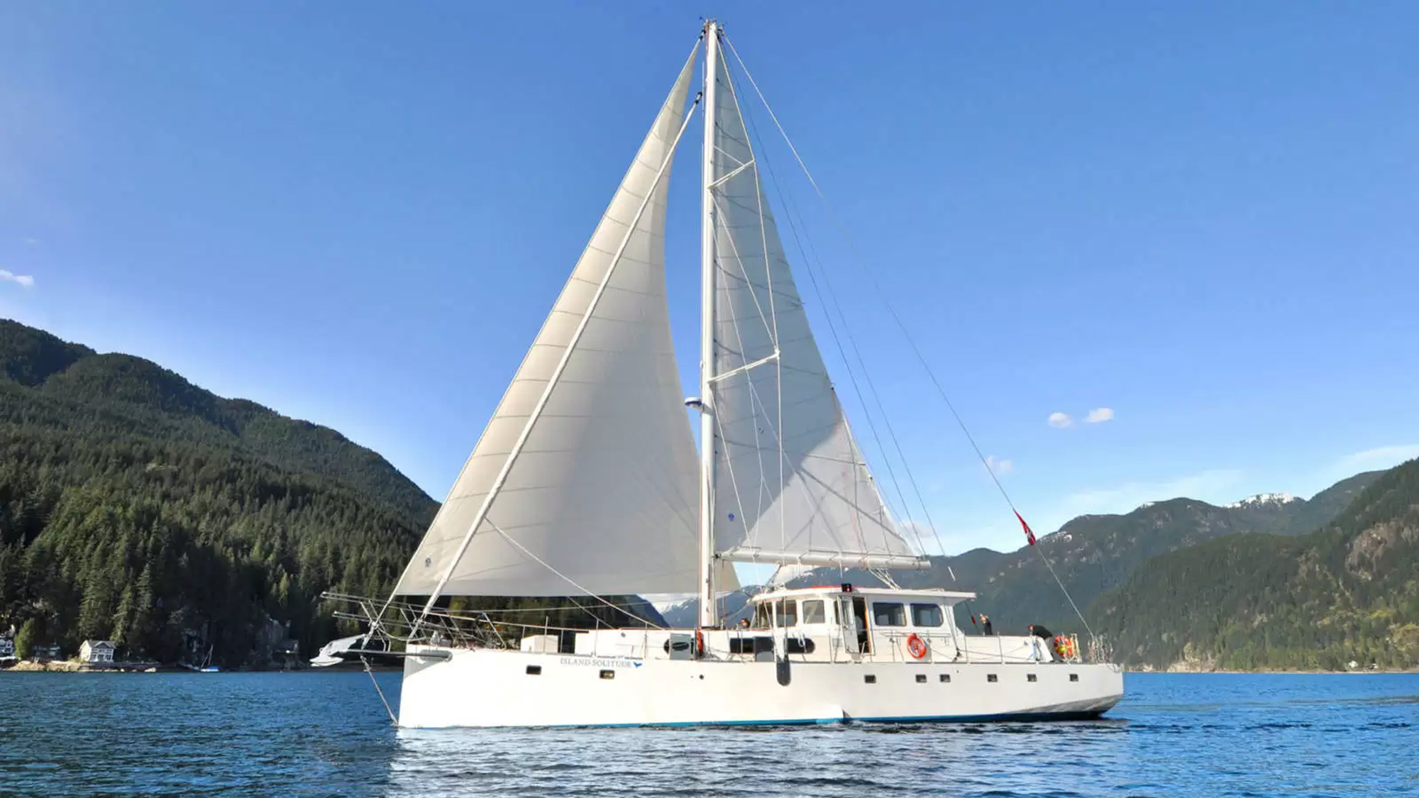 Island Solitude Sailing Catamaran in Alpine Lake A stunning white sailing catamaran with full sails deployed on a pristine alpine lake, surrounded