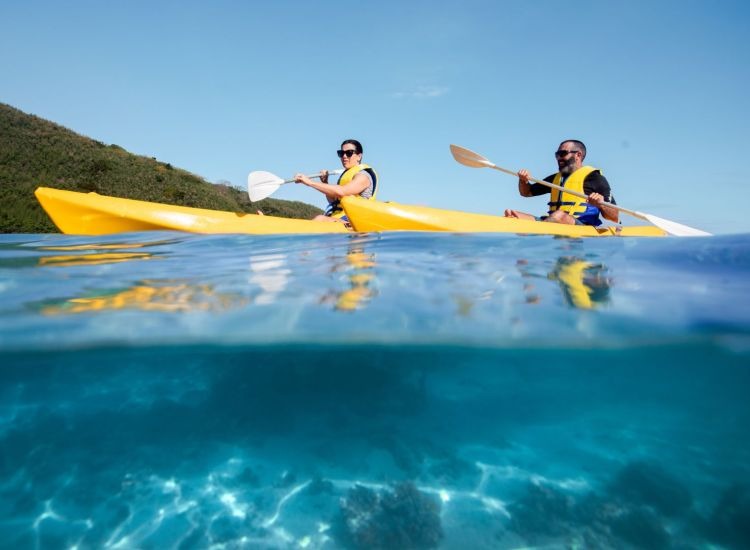 Two kayakers in bright yellow tandem kayaks paddle through crystal-clear turquoise waters with