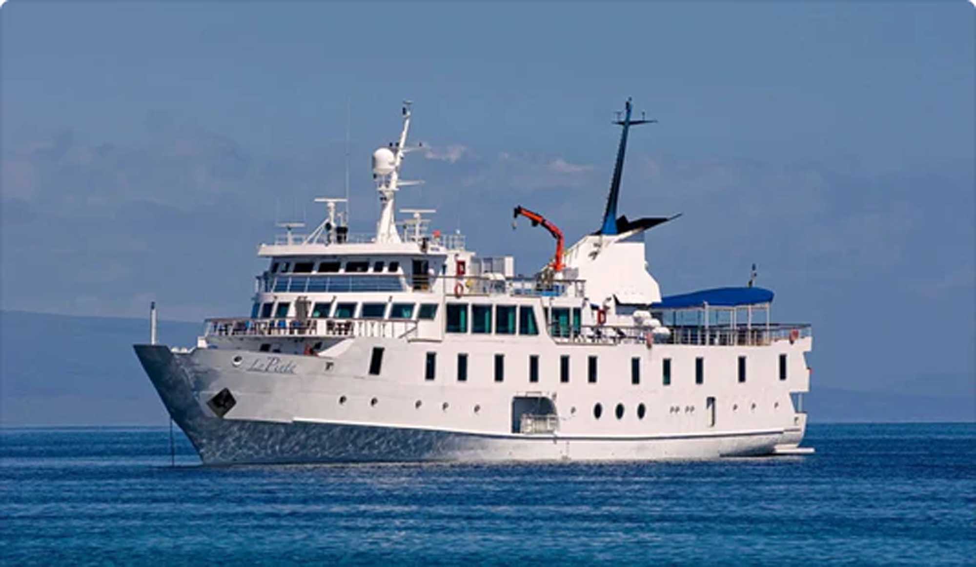 A white-hulled expedition cruise vessel, La Pinta, anchored in calm blue waters. The ship features