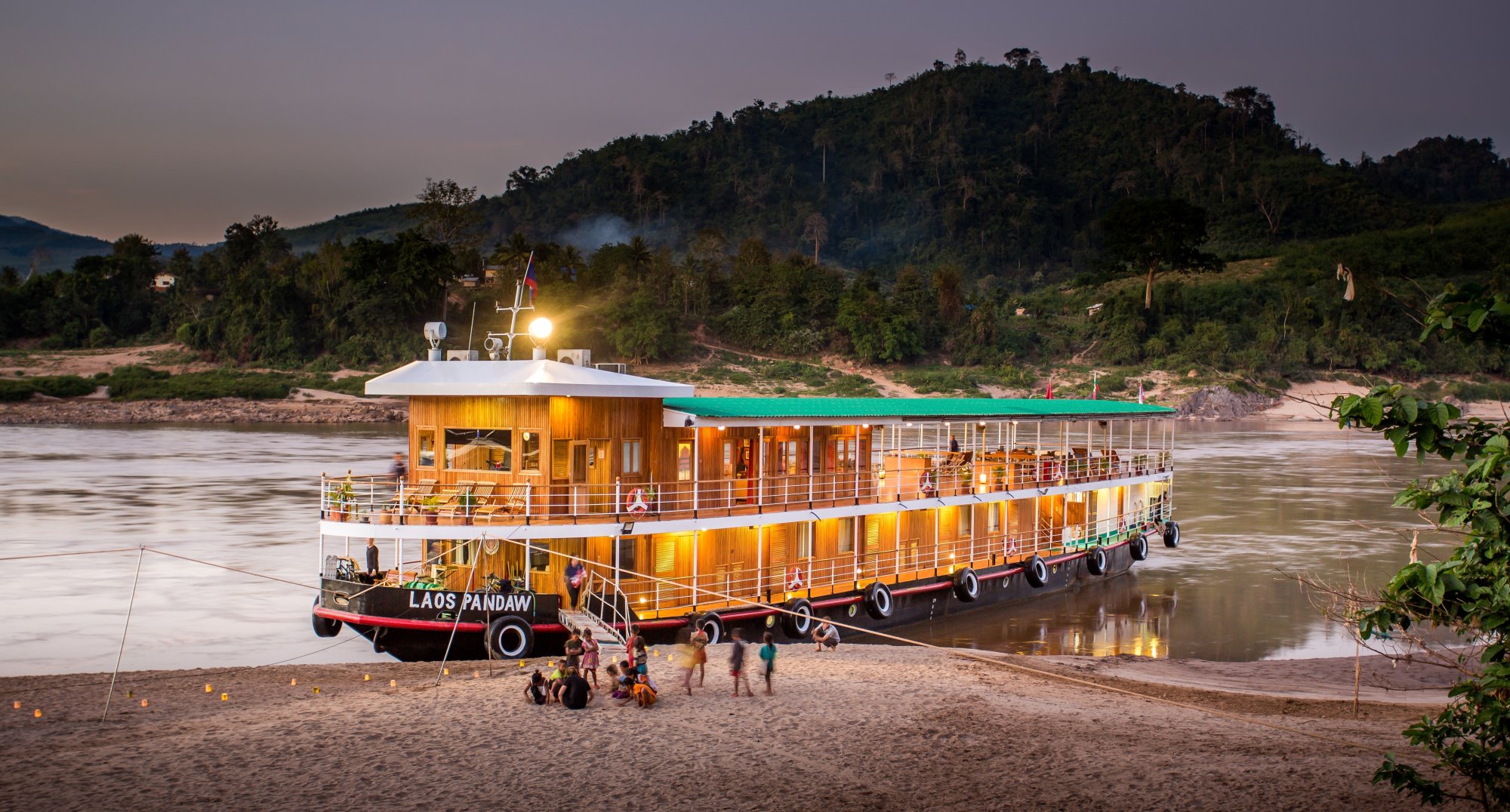 The Laos Pandaw, a distinctive golden-hulled river cruise vessel, is moored along a sandy riverbank
