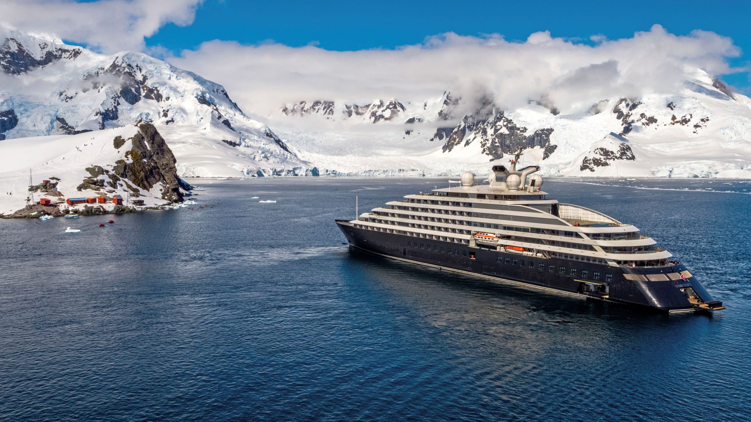 A modern expedition cruise ship anchors in pristine Antarctic waters near a research station