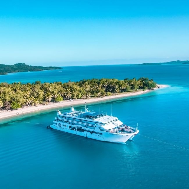 A modern multi-deck cruise ship anchors in crystalline turquoise waters off a pristine tropical