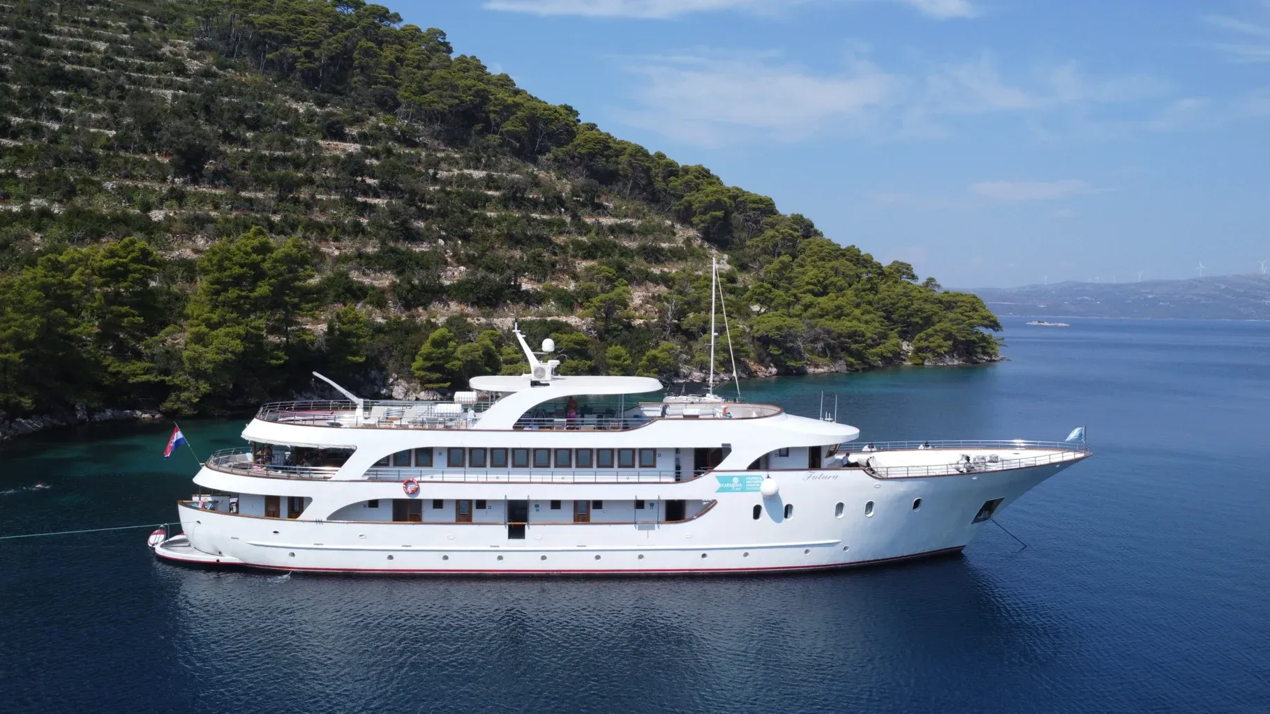 Luxury Expedition Yacht Anchored in Mediterranean Cove A pristine white multi-deck expedition yacht is anchored in crystal-clear turquoise waters beneath