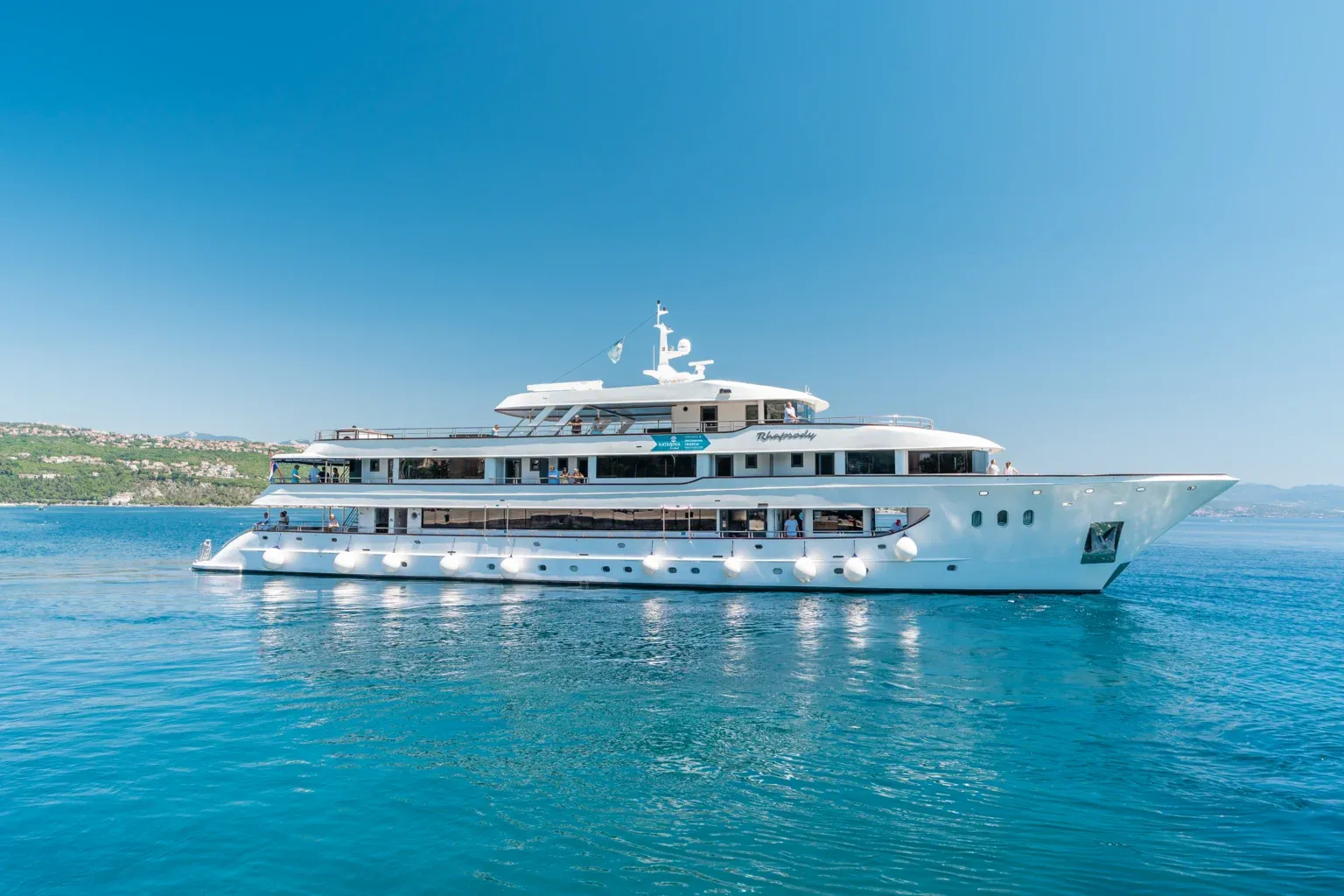 Luxury Expedition Yacht Rhapsody at Anchor A pristine white luxury expedition yacht anchored in crystal-clear turquoise waters with a lush