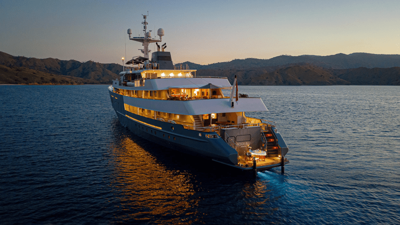 A beautifully illuminated luxury expedition yacht anchored in calm turquoise waters at dusk