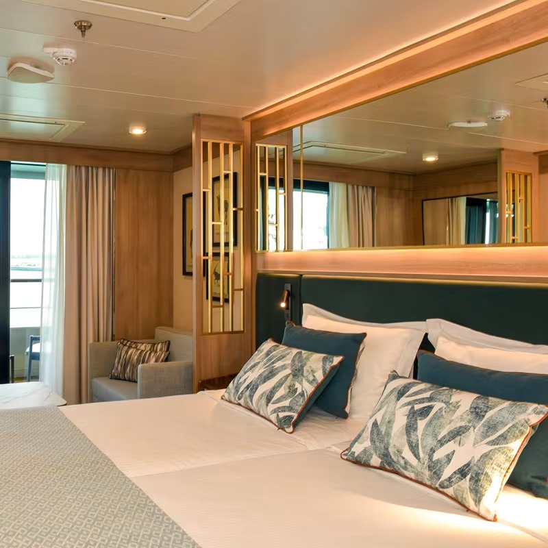 Luxury Veranda Suite Stateroom with Ocean View An elegantly appointed cruise ship veranda suite featuring warm wood paneling, a king-sized bed