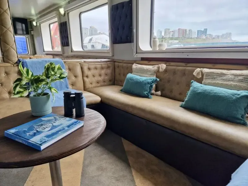 Luxury Yacht Lounge with Coastal City View An elegant interior lounge aboard a luxury yacht or expedition vessel, featuring beige tufted