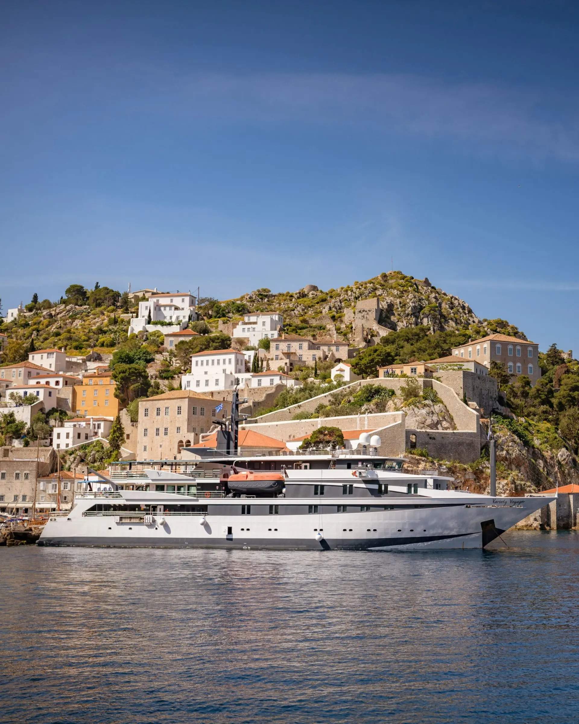 A sleek, modern motor yacht with white and dark hull is anchored in clear blue waters adjacent to