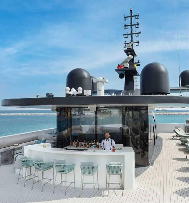 Luxury Yacht Sky Deck Bar with Turquoise Waters An elegant outdoor bar and lounge area on the sky deck of a luxury expedition yacht, featuring