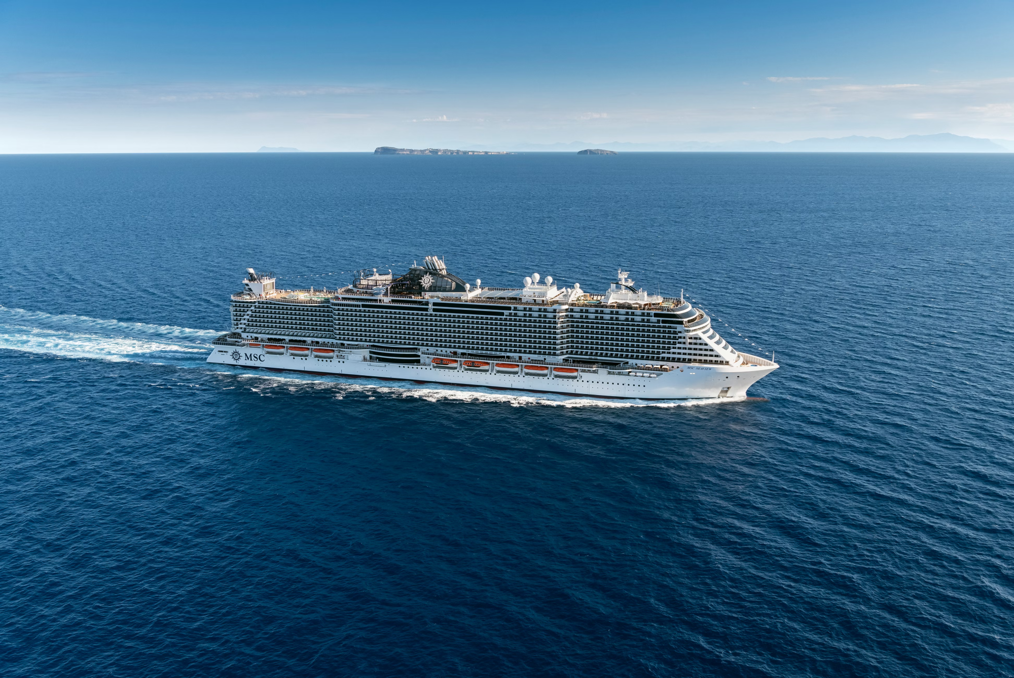 MSC Cruise Ship at Sea with Distant Islands A large modern cruise ship operated by MSC Cruises sails through open ocean waters under clear blue