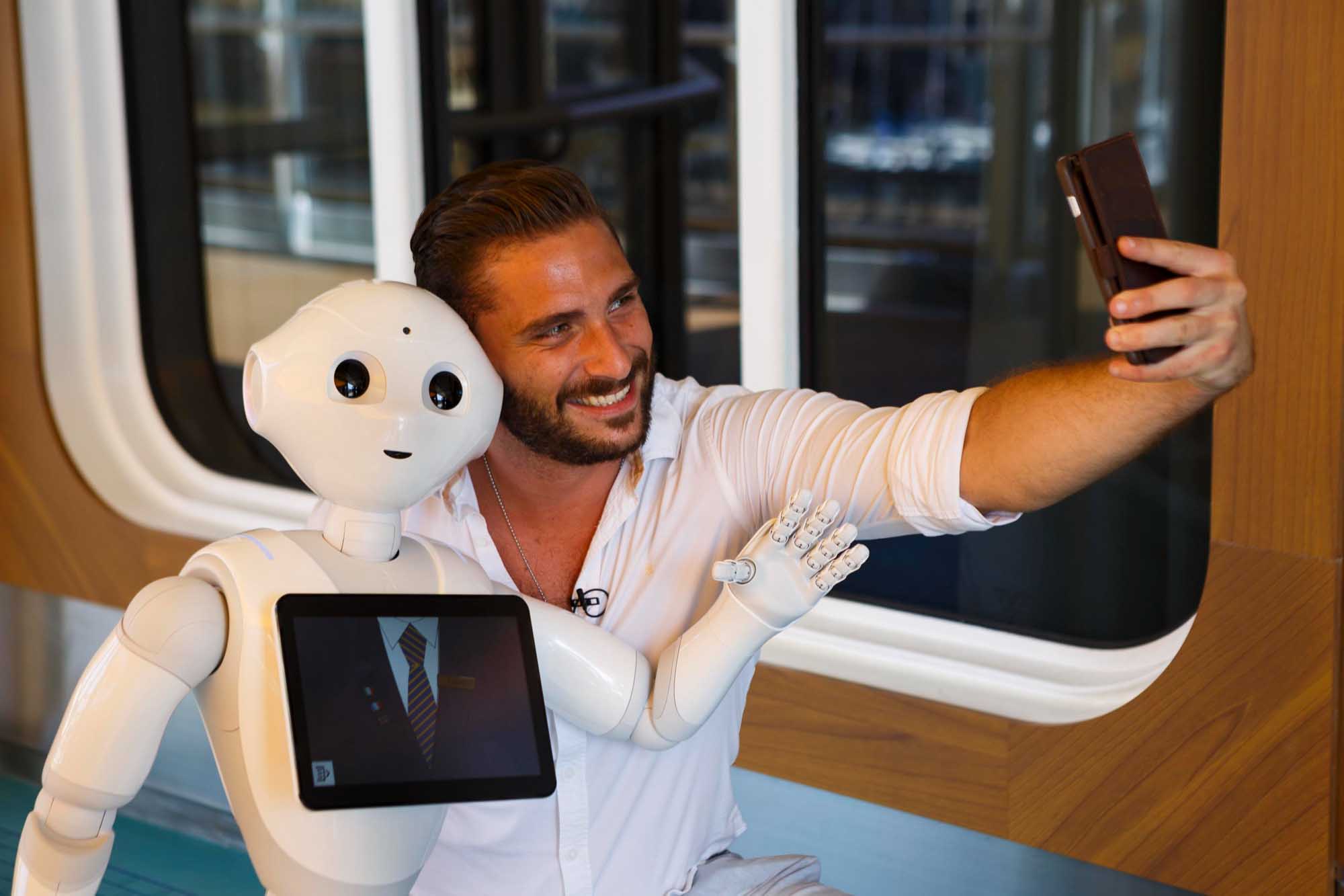 Man Taking Selfie with Humanoid Robot A smiling man in a white shirt takes a selfie with a white humanoid robot featuring a friendly face