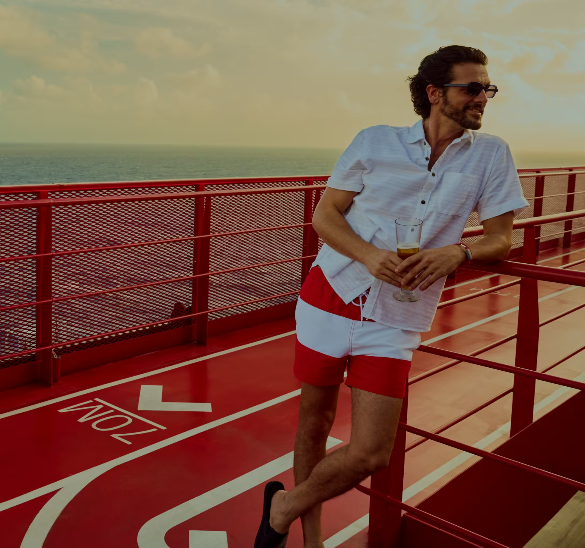 Man on Virgin Voyages Ship Deck at Sea A man in a light blue short-sleeved shirt and red shorts stands on the red and white deck of