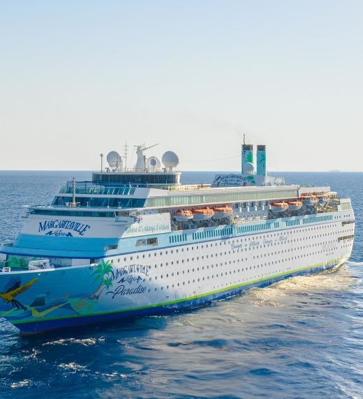 Two large cruise ships are docked side by side in calm blue ocean waters. The foreground vessel