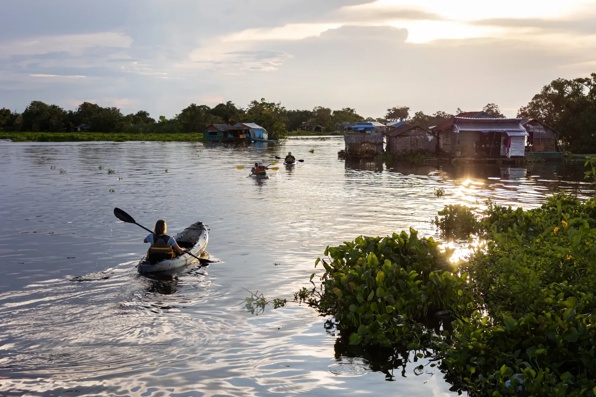 A kayaker paddles through calm waters of the Mekong River near a traditional floating village