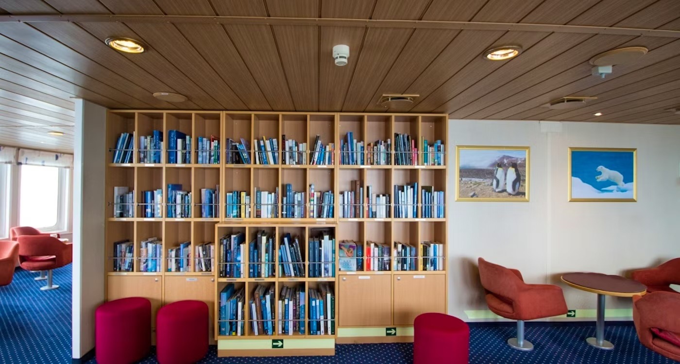 Modern Ship Library with Arctic-Themed Artwork A contemporary library lounge aboard a cruise ship, featuring extensive wooden shelving filled