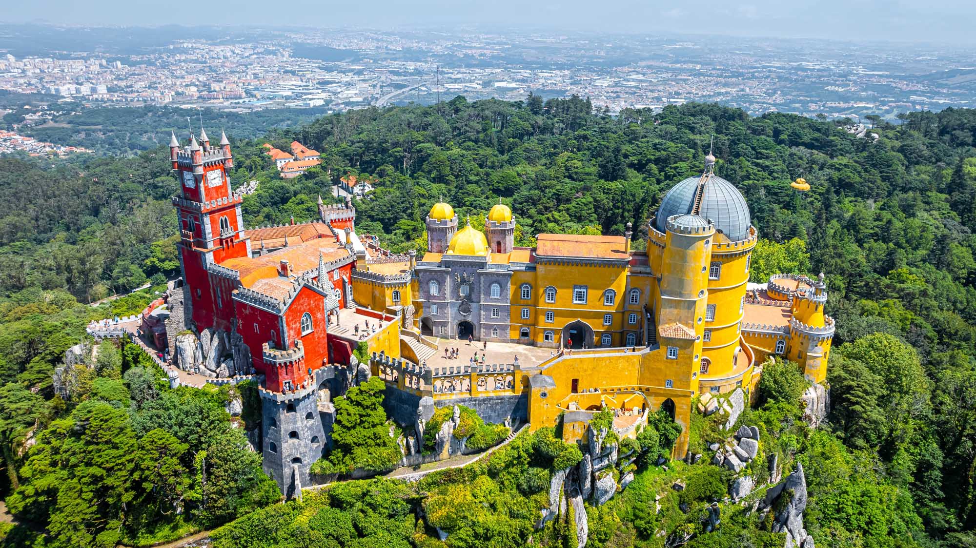 Pena Palace Sintra Portugal Aerial View A dramatic aerial photograph of the iconic Pena Palace perched atop a forested hilltop in Sintra