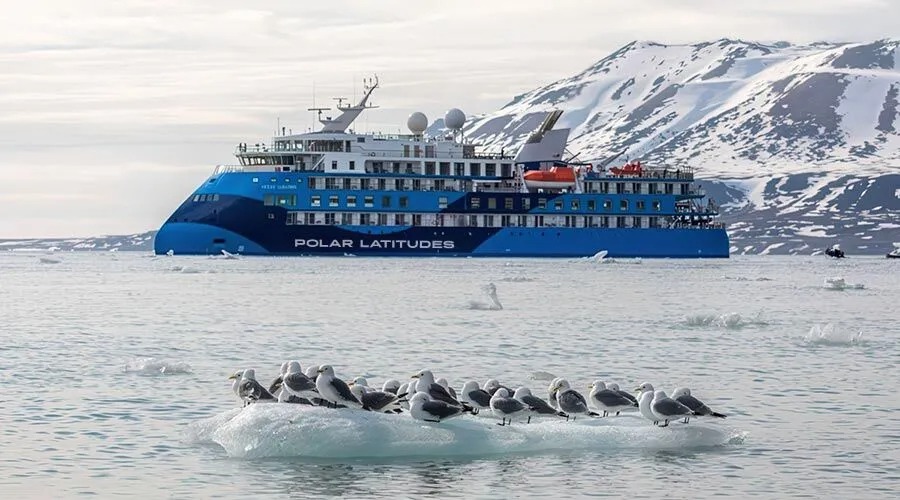 The Polar Latitudes expedition cruise ship navigates Arctic waters near snow-covered mountains