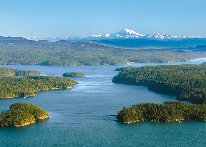 Puget Sound Aerial View with Snow-Capped Mountains An aerial photograph of Puget Sound in Washington State, showcasing forested islands, calm blue