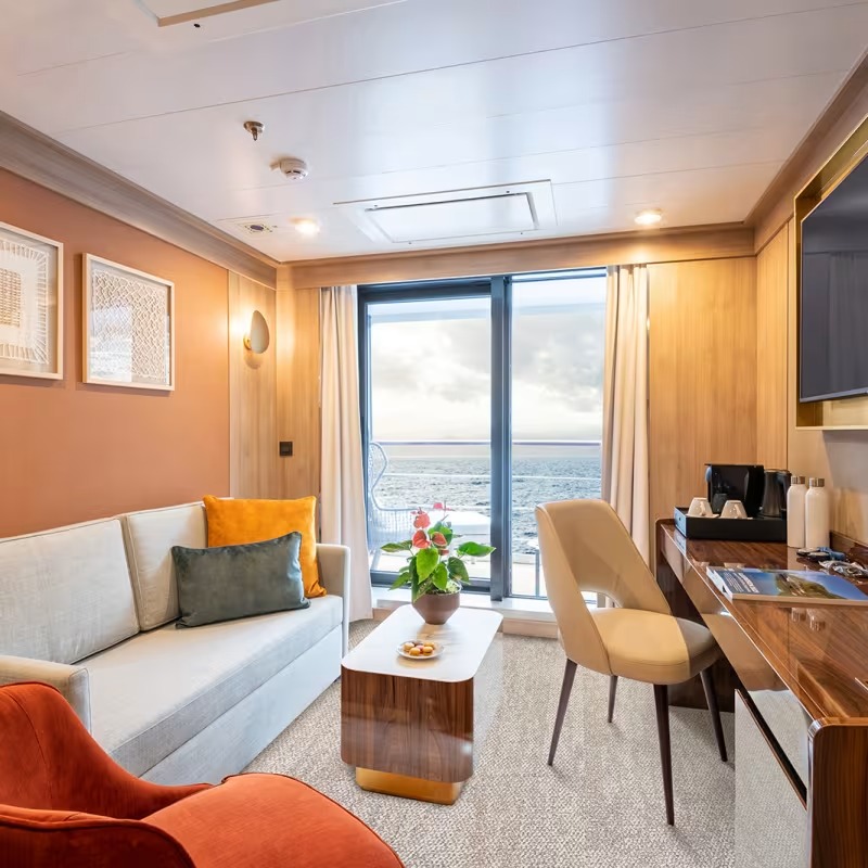 Quark Expeditions Deluxe Suite with Ocean View A luxurious deluxe suite aboard a Quark Expeditions vessel featuring warm orange and wood-tone
