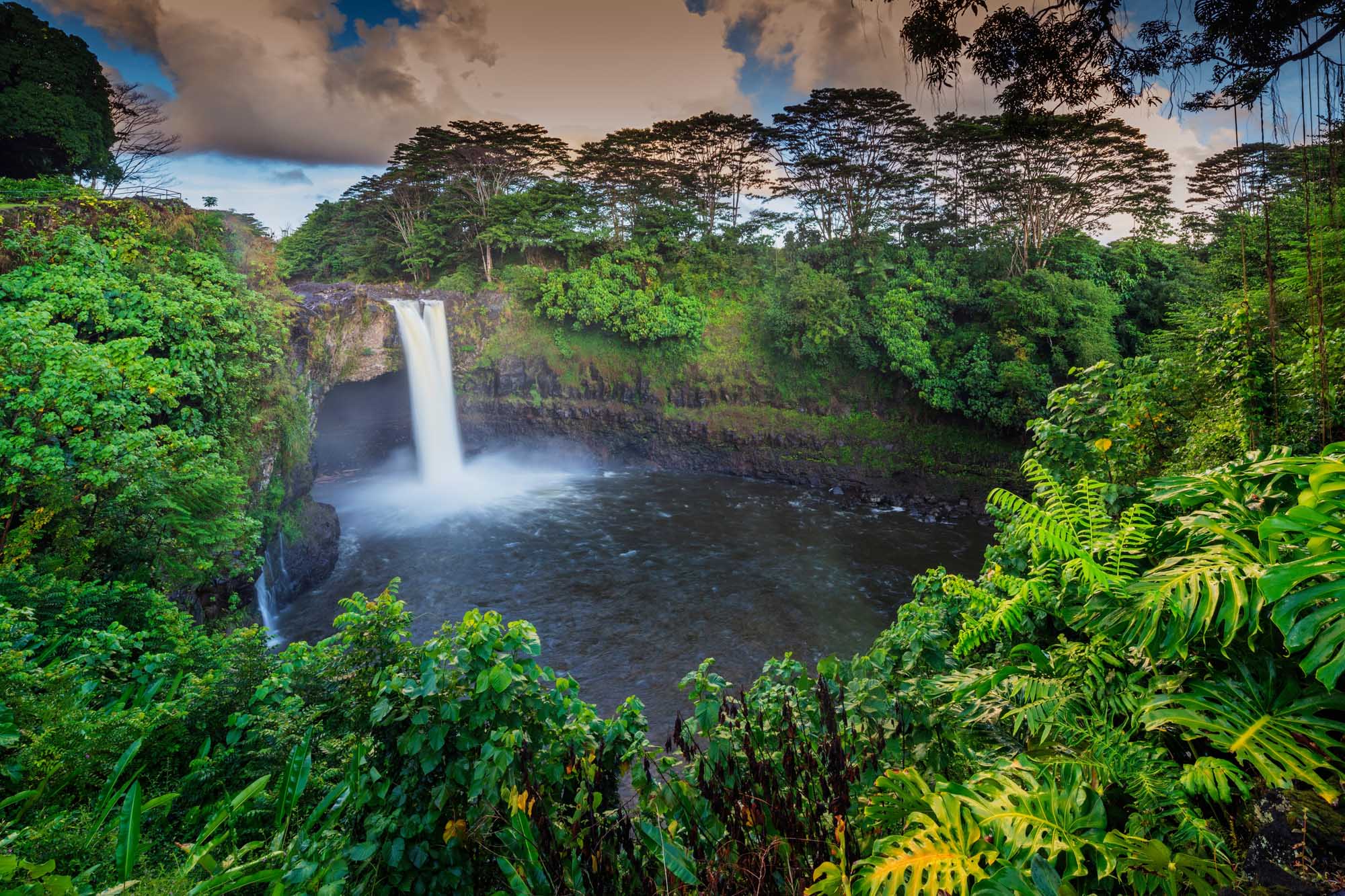 Rainbow Falls, Big Island Hawaii A stunning waterfall cascades into a dark pool surrounded by lush tropical rainforest vegetation