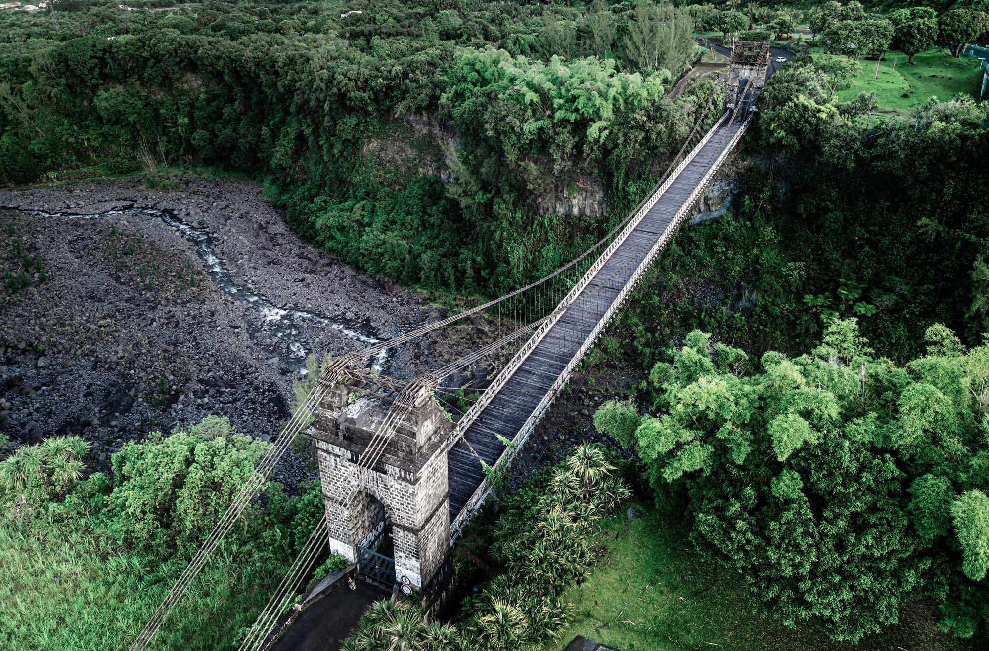 Sainte-Anne Suspension Bridge Over Tropical Forest An aerial view of a long wooden suspension bridge spanning across a lush, dense tropical forest