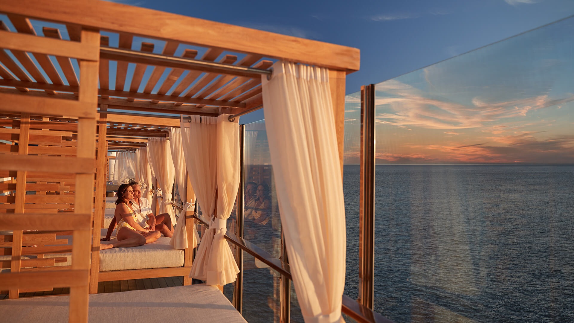 Scenic Deck Cabanas with Ocean Sunset View An elegant outdoor cabana area featuring wooden pergolas with flowing cream-colored curtains