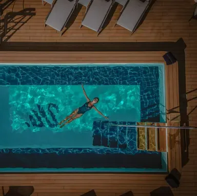 Snorkeler Exploring Turquoise Waters from Deck An overhead view of a snorkeler in vibrant turquoise water near a wooden deck with lounge chairs