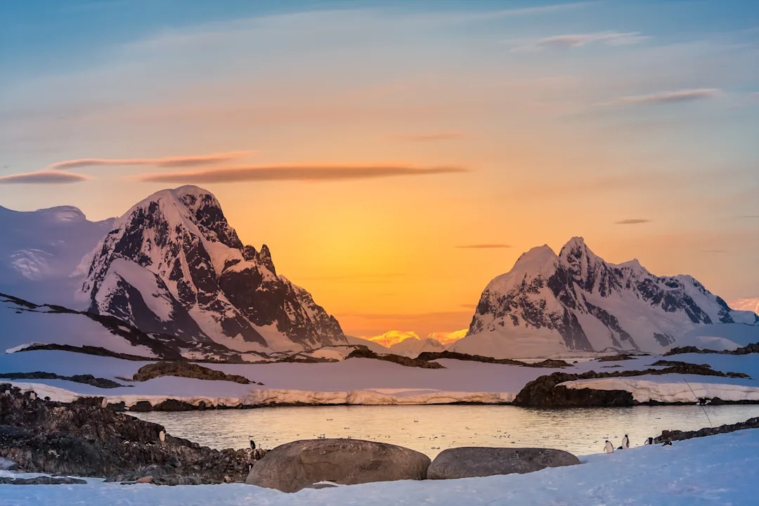 Snow-Capped Mountains at Sunset in Antarctica A breathtaking polar landscape featuring towering snow-covered mountain peaks framed by golden
