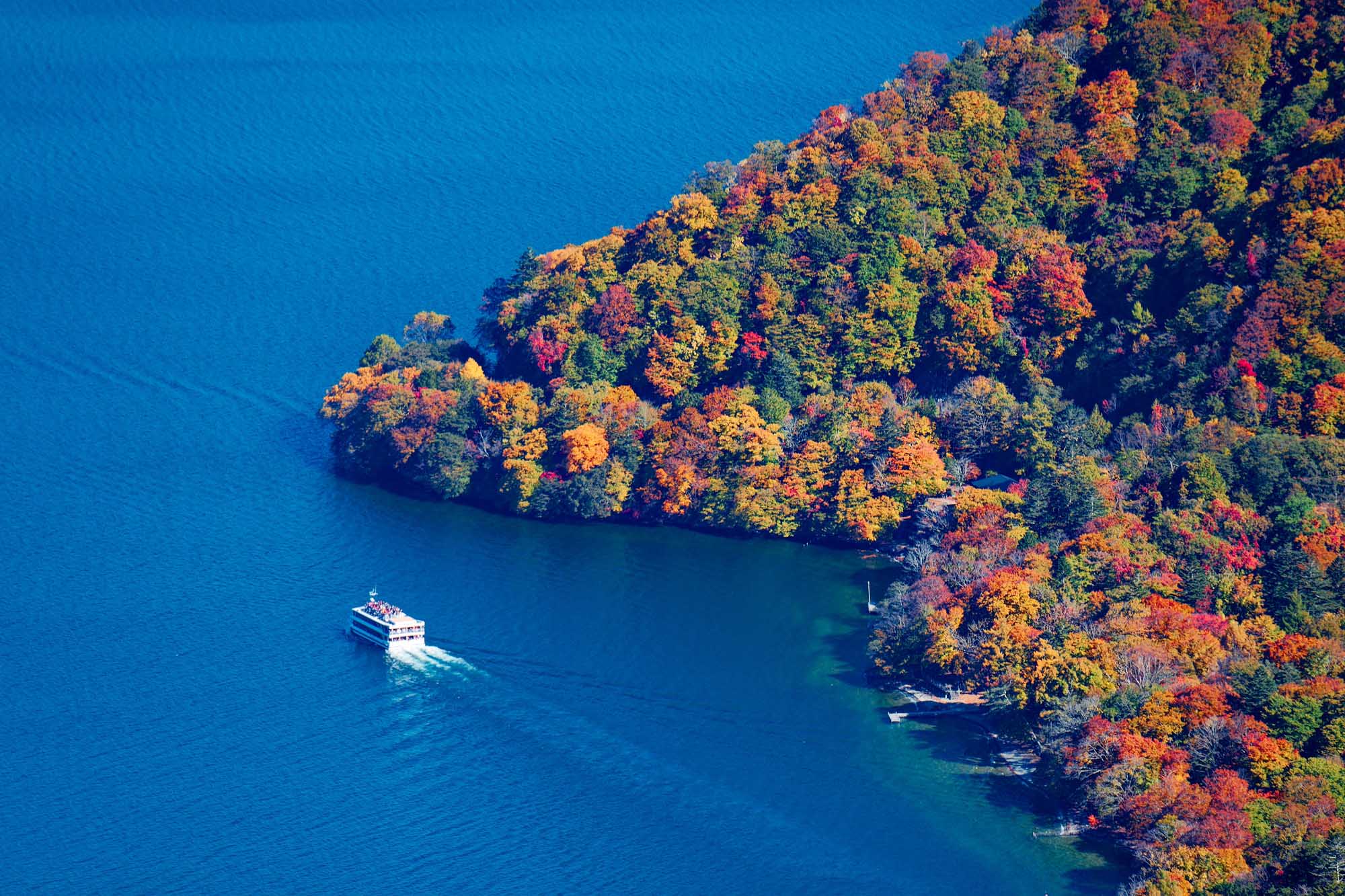 Tour Boat on Lake Chuzenji with Autumn Foliage An aerial view of a tour boat cruising on the pristine blue waters of Lake Chuzenji in Nikko
