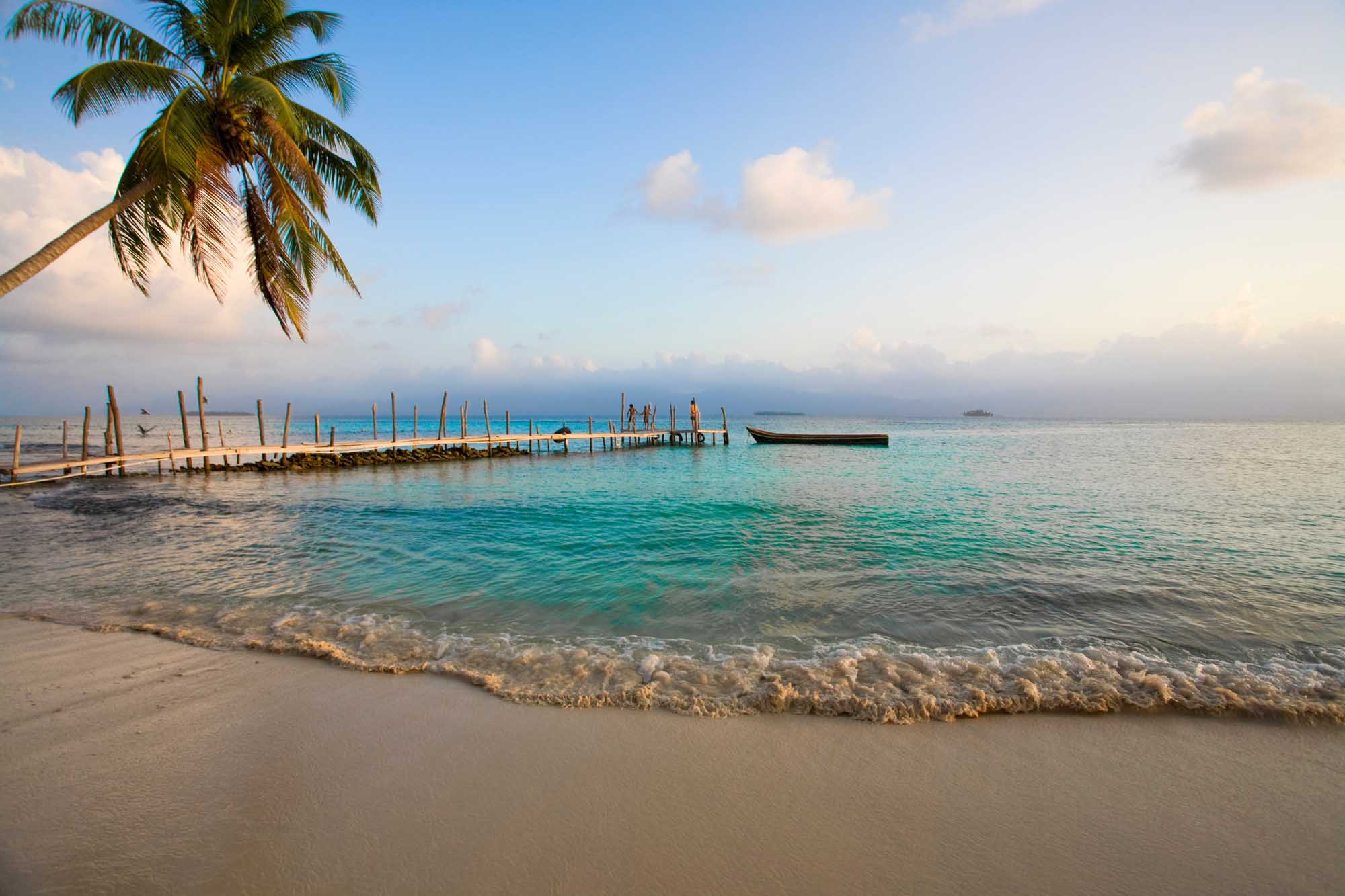 Tropical Beach with Wooden Pier and Moored Boat A pristine tropical beach scene featuring turquoise waters, white sand, and a traditional wooden