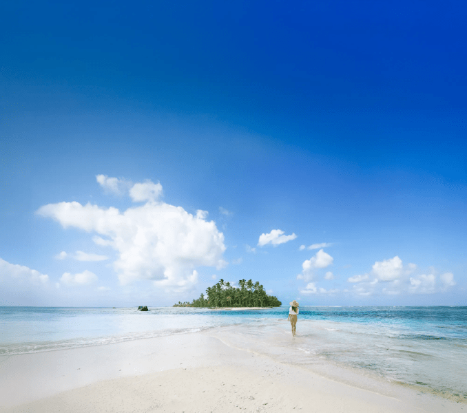 A pristine tropical beach scene featuring white sand, crystal-clear turquoise waters, and a small